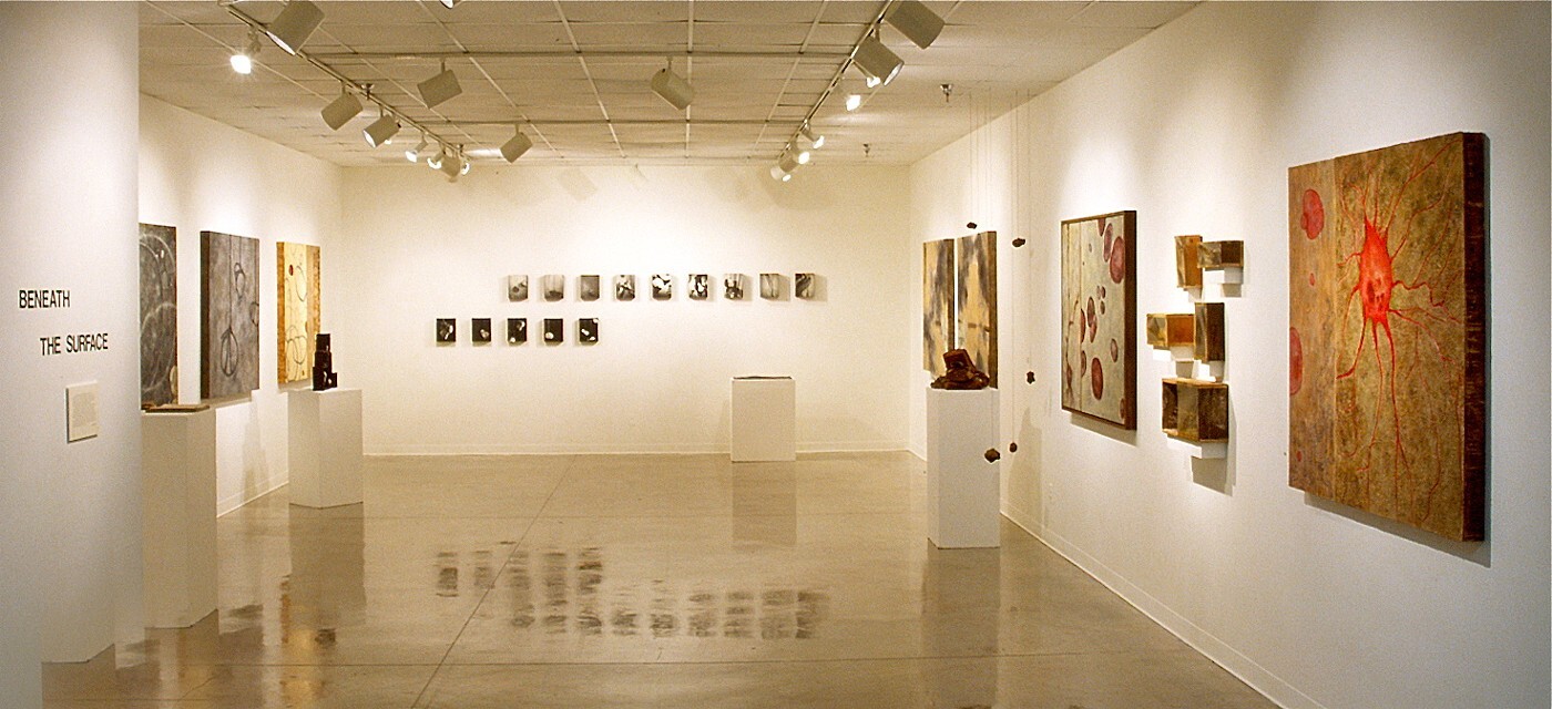 Multiple paintings hung on three white walls within the Palo Verde Graduate Gallery space with multiple sculptures on plinths set up around the room.